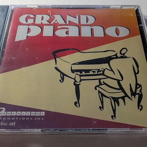 May include: A CD case with the words "GRAND PIANO" in large white letters over a red and yellow background. The image features a black and white illustration of a person playing a grand piano. The CD case is a 2 disc set from Cornerstone Promotions, Inc.
