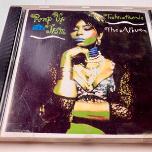 Könnte beinhalten: Eine CD-Hülle mit dem Album "Pump Up the Jam" von Technotronic. Das Cover zeigt eine Frau mit blauem Lippenstift und grünen Akzenten, geschmückt mit Schmuck. Der Albumtitel und der Künstlername sind in einer stilisierten Schriftart dargestellt.