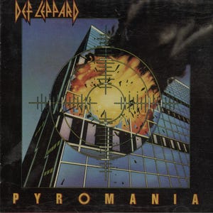 Könnte beinhalten: CD-Hülle des Def Leppard-Albums "Pyromania". Das Cover zeigt ein Hochhaus, das von einem Fadenkreuz anvisiert wird, mit einer Explosion in der Mitte. Das Logo der Band befindet sich oben, der Albumtitel unten.