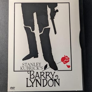 以下が含まれることがあります： スタンリー・キューブリック・コレクションの映画『バリー・リンドン』のDVDケース。カバーには、白い背景にブーツを履いてピストルを持つ人物の黒いシルエットが描かれており、赤いバラの花とタイトルがその下に印刷されています。