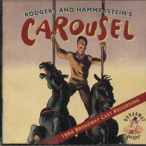 May include: CD case for the 1994 Broadway Cast Recording of Rodgers and Hammerstein's "Carousel." The cover features a man holding poles above two black carousel horses. The title is in red, with the Broadway Angel logo.