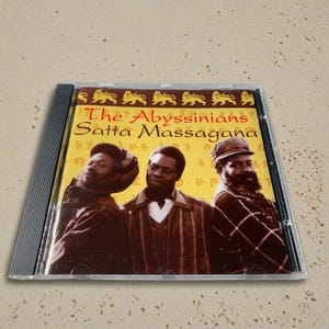 May include: A CD case featuring the album "Satta Massagana" by The Abyssinians. The cover art displays three men in brown and black clothing against a yellow background. The album title is in red.