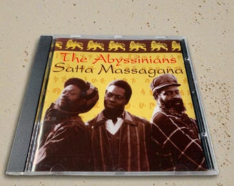 Może przedstawiać: Pudełko CD z albumem "Satta Massagana" zespołu The Abyssinians. Okładka przedstawia trzech mężczyzn w brązowych i czarnych ubraniach na żółtym tle. Tytuł albumu jest czerwony.