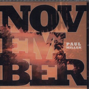 Peut inclure: Boîtier de CD avec le mot "NOVEMBER" en grandes lettres noires, partiellement superposé à un paysage de coucher de soleil. Le nom de l'artiste, "PAUL MILLER", est visible. L'ensemble est dominé par des tons chauds, orangés et bruns.