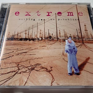 Op de afbeelding: CD-hoesje voor het album "Waiting for the Punchline" van Extreme. De cover toont een persoon in een blauw clownskostuum in een verlaten landschap met industriële structuren op de achtergrond. De bandnaam staat in roze letters.