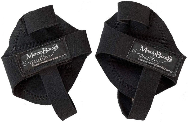 May include: A pair of black finger protectors with a label that reads "Marcia Baradi Quilter" and a website address. The protectors are made of a soft, flexible material and have a textured surface.
