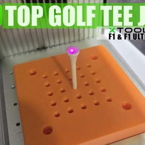 Peut inclure: Un gabarit de tee de golf orange avec un tee en bois au centre. Le tee est éclairé par une lumière violette. Le gabarit a une grille de trous pour aligner le tee.