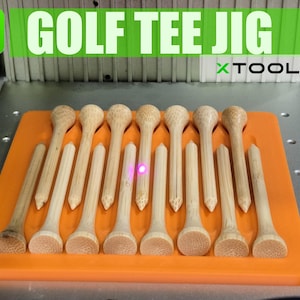 May include: A golf tee jig with wooden golf tees of varying lengths. The tees are arranged on an orange platform, with the text "GOLF TEE JIG" and "XTOOL F1" visible. The XTOOL logo is in the upper left corner.
