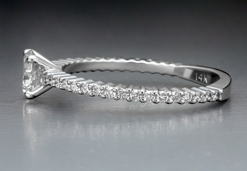 May include: A silver ring with a single diamond set in the center and a row of smaller diamonds around the band. The band is textured and marked "14K".