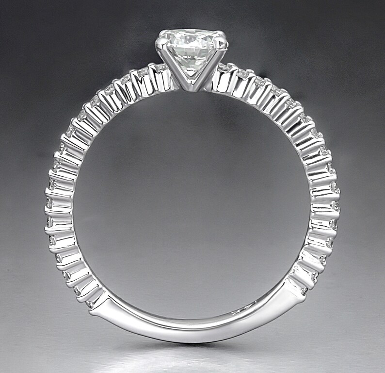 May include: A silver ring with a single, round diamond set in a prong setting. The band is decorated with a row of smaller diamonds.
