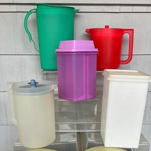 May include: A collection of five plastic kitchen containers including a green pitcher with a handle, a red pitcher with a handle, a purple rectangular canister with a lid, a translucent pitcher with a blue center lid, and a white rectangular canister.