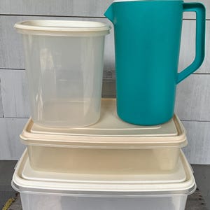 May include: A collection of kitchen storage containers including a tall, translucent cylindrical container with a white lid, a teal pitcher with a white lid, and two rectangular, translucent storage containers with matching white lids.