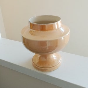 Op de afbeelding: Een lichtoranje keramische vaas met een brede basis en een rond lichaam. De vaas heeft een gladde, glanzende afwerking.