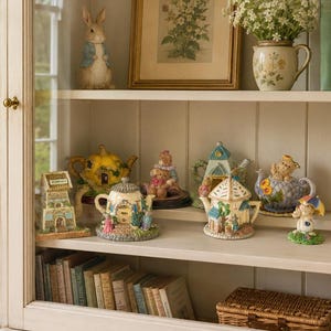May include: A white wooden display cabinet filled with decorative items including a rabbit figurine, a framed botanical print, a ceramic pitcher with white flowers, and several miniature house-shaped teapots and figurines on the shelves.