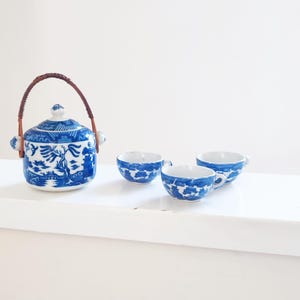 May include: A blue and white porcelain tea set with a teapot and three cups. The teapot has a brown handle and a lid. The cups have a blue and white floral pattern.