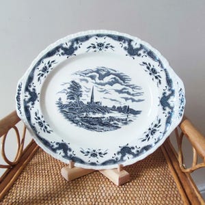 May include: A white oval serving platter with a blue and white floral border and a black and white scene of a church and trees in the center.