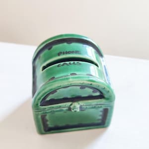 Può includere: Porta telefono in ceramica verde a forma di forziere con accenti neri e le parole "Phone Calls" scritte sul davanti.