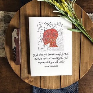 May include: A greeting card with a quote and a graphic of a head filled with gears and mathematical symbols. The card is on a wooden tray with a corkscrew and yellow floral accents.
