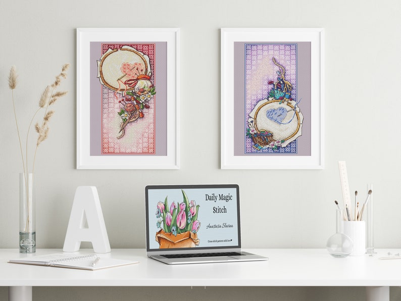 May include: Two framed cross-stitch artworks with floral and embroidery hoop designs. A laptop displays the text "Daily Magic Stitch" and a bouquet of tulips. The scene is set on a white desk with decorative elements.