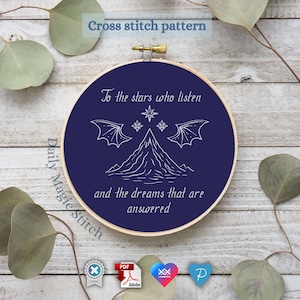 Op de afbeelding: Een blauwe borduurring met witte draad die een berg, sterren en vleugels voorstelt. De tekst "To the stars who listen and the dreams that are answered" is geborduurd op de ring.