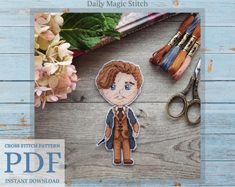 May include: Cross stitch pattern PDF download of a cartoon illustration of a young man with brown hair, wearing a brown suit and a blue tie, holding a wand. The background is a wooden surface with embroidery floss and scissors.