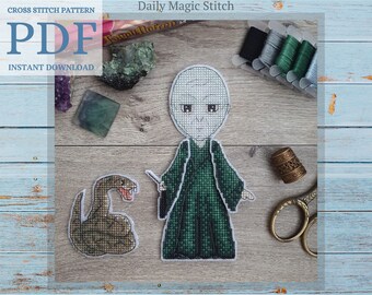 May include: Cross stitch pattern PDF download of a cartoon character with a snake. The character is wearing a green robe and has a wand in their hand. The snake is brown and has a green tongue. The pattern is on a wooden background with a few colorful stones.