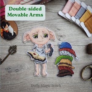 May include: Two cross-stitch figures of a character with large ears and a stack of hats. The figure with large ears is holding a book and a sock. The other figure is a stack of hats. The text "Double-sided Movable Arms" is in a green box.