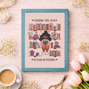 May include: A framed cross-stitch depicting a person reading, with bookshelves filled with books and decorative items. The text reads "Spending Time With" and "My Book Boyfriends". The frame is teal, and the background is a light pink.