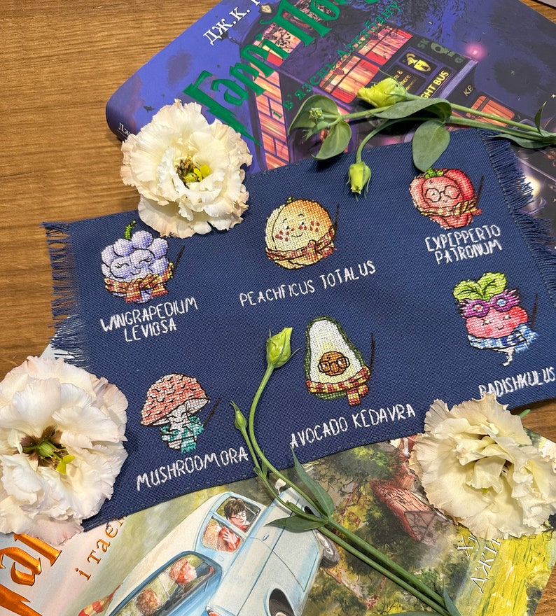 May include: A navy blue embroidered fabric with various fruit and vegetable designs, each holding a wand. The text includes "WINGRAPEDIUM LEVIOSA", "PEACHFICUS TOTALUS", "EXPEPPERTO PATRONUM", "MUSHROOMORA", "AVOCADO KEDAVRA", and "RADISHKULUS".