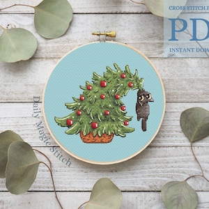 May include: A cross stitch pattern featuring a black cat peeking out from behind a green Christmas tree with red baubles. The pattern is in a blue hoop and the text "Daily Magic Stitch" is written on the left side of the hoop.