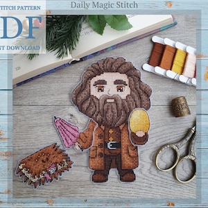 Op de afbeelding: PDF-patroon voor kruissteek voor een personage met bruin haar en een baard, dat een gouden ei en een paraplu vasthoudt. Het personage draagt een bruine jas en een zwarte riem. Het patroon heeft de titel "Daily Magic Stitch".