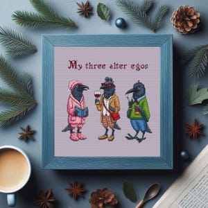 Op de afbeelding: Een kruissteekpatroon met drie kraaien met verschillende persoonlijkheden. De tekst "Mijn drie alter ego's" staat boven de kraaien. De kraaien dragen verschillende outfits, waaronder een roze badjas, een geruit overhemd en een groene trui.
