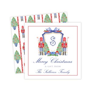 May include: A square gift tag featuring a blue crest with the letter S, flanked by two nutcrackers and Christmas trees. Below, the text reads Merry Christmas A GIFT FROM The Sullivan Family. The background shows a pattern of trees and nutcrackers.