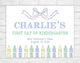 Puede incluir: Un cartel blanco con un lazo de cinta azul y el texto "CHARLIE'S FIRST DAY OF KINDERGARTEN" en azul y verde. Debajo del texto está "Mrs. Robinson's Class August 30, 2023" en negro. La parte inferior del cartel tiene una fila de 10 lápices de colores.