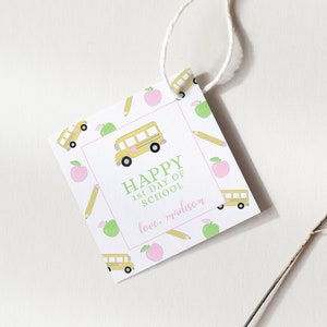 May include: A square gift tag with a white background and a repeating pattern of yellow school buses, green apples, and yellow pencils. The tag features the text "HAPPY 1st DAY OF SCHOOL" in green, with "love, madison" in pink.