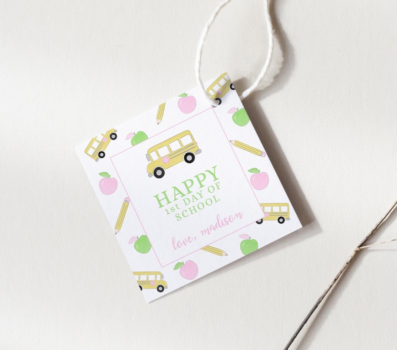 May include: A square gift tag with a white background and a repeating pattern of yellow school buses, green apples, and yellow pencils. The tag features the text "HAPPY 1st DAY OF SCHOOL" in green, with "love, madison" in pink.