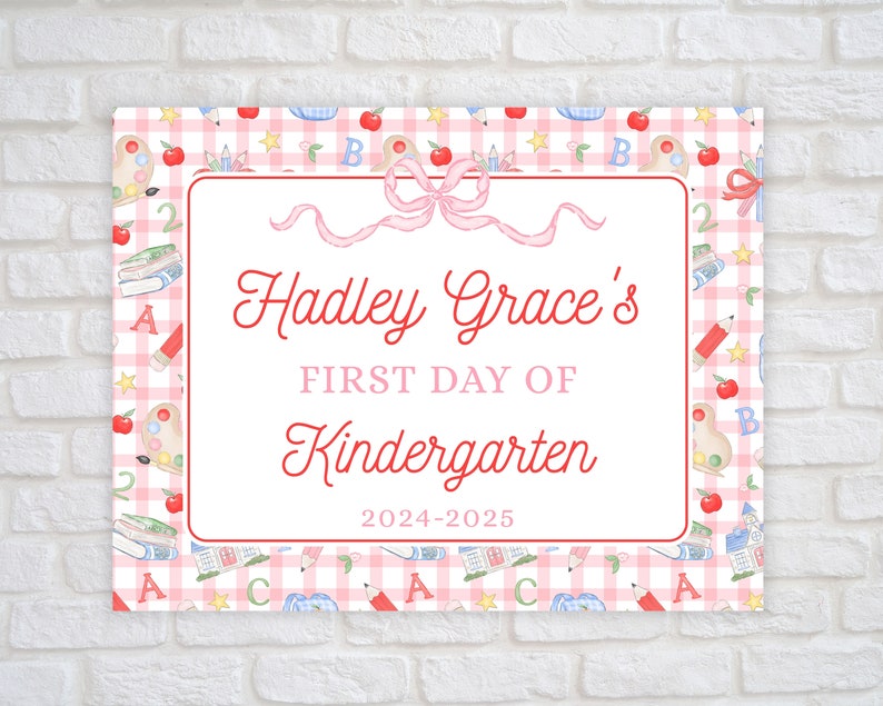 May include: A pink and white gingham patterned sign with a red border. The sign says "Hadley Grace's First Day of Kindergarten 2024-2025". The sign is decorated with a pink bow, apples, pencils, books, and stars.