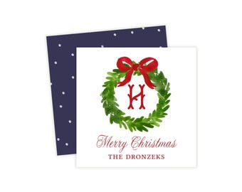 Könnte beinhalten: Eine quadratische weiße Karte mit einem aquarellierten grünen Kranz, einer roten Schleife und dem Buchstaben H in der Mitte. Unter dem Kranz steht der Text Merry Christmas und THE DRONZEKS. Dahinter liegt eine dunkelblaue Karte mit weißen Punkten.