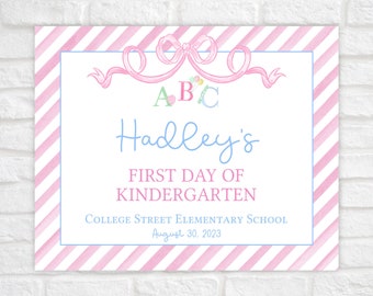 May include: Pink and white striped sign with a pink bow and the letters A, B, and C. The sign says "Hadley's First Day of Kindergarten" and "College Street Elementary School August 30, 2023".