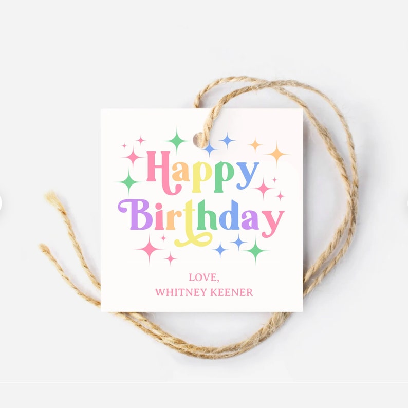 May include: A white gift tag with a rainbow colored "Happy Birthday" message surrounded by colorful stars. The tag has a hole at the top and is tied with twine. The text "LOVE, WHITNEY KEENER" is printed in pink at the bottom of the tag.