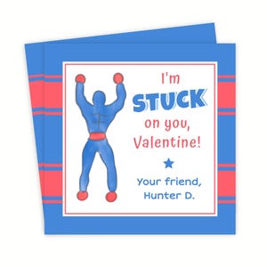 May include: A Valentine's Day card with a blue and red design. The card features a blue superhero figure with red accents, and the text "I'm STUCK on you, Valentine!" is displayed. The card is signed "Your friend, Hunter D."