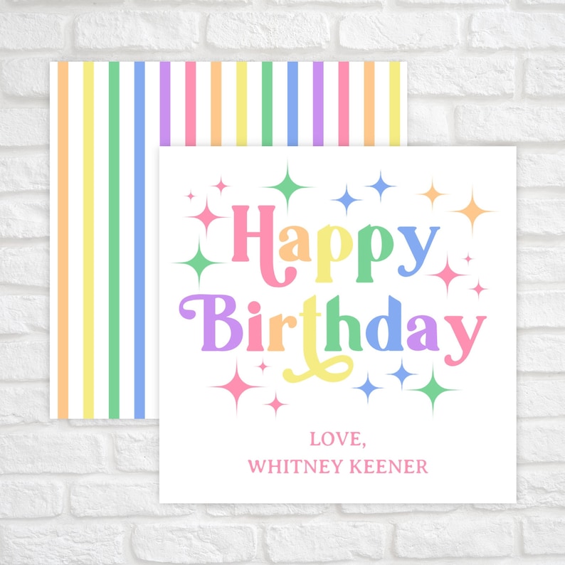 May include: A white card with the text "Happy Birthday" in rainbow colors with stars around the text. The card has the text "Love, Whitney Keener" at the bottom. The card is on a white brick background with a rainbow striped paper behind it.