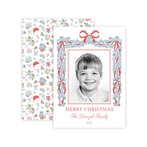 May include: A Christmas card featuring a black and white photo of a child framed by a red border and floral garland. The card reads "MERRY CHRISTMAS" and "The Dronzek Family 2025". The envelope has a floral pattern with Santa hats.