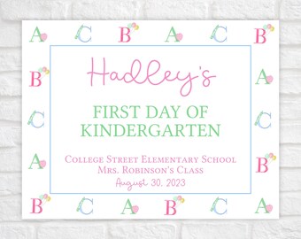 May include: A printable sign for a child's first day of kindergarten. The sign is white with a blue border and features the name "Hadley's" in pink cursive lettering. The text "First Day of Kindergarten" is in green lettering. The sign also includes the school name, teacher's name, and date.