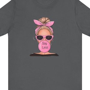 May include: A dark gray t-shirt with a graphic of a woman with pink hair and sunglasses blowing a bubble that says "Say Less".