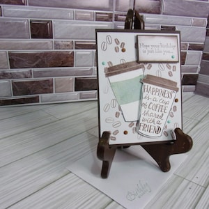 May include: A brown card with a coffee cup design and the text "Happiness is a cup of coffee shared with a friend". The card is on a wooden easel and has a small brown tag with the text "Hope your birthday is just like you..."