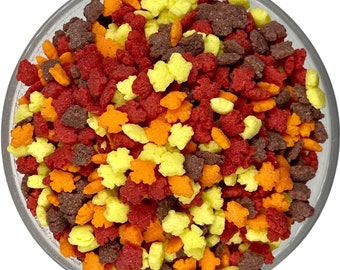 May include: A bowl of colorful fall-themed sprinkles. The sprinkles are shaped like leaves and are in shades of red, orange, yellow, and brown.