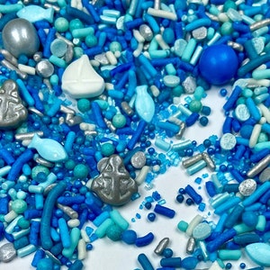 May include: Blue and silver sprinkles with various shapes, including fish, anchors, and sailboats. The sprinkles are scattered on a white background.