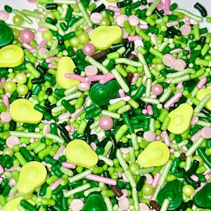 Puede incluir: Una mezcla de sprinkles verdes, rosas y marrones en forma de mitades de aguacate, bolitas pequeñas y palitos largos y delgados.