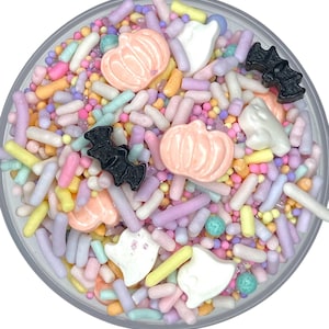 May include: A clear container filled with colorful Halloween-themed sprinkles. The sprinkles include pastel-colored rods, small round sprinkles, and candy shapes of pumpkins, ghosts, and bats. The colors include pink, orange, yellow, purple, and green.